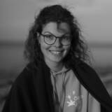 Frau mit Brille lächelt am Strand.