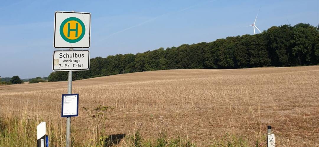 Bushaltestellenschild vor Feldlandschaft