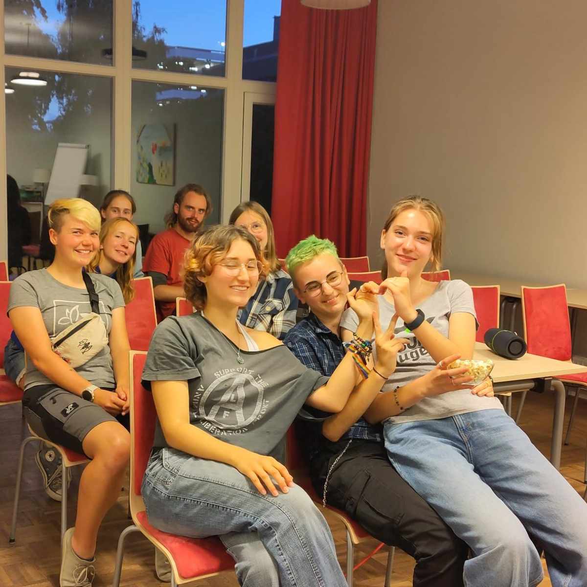 Gruppe junger Leute in einem Raum mit roten Stühlen.