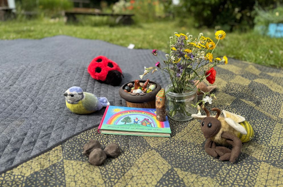 Picknickdecke mit Blumen, Kinderbuch und Stofftieren im Garten